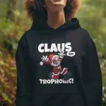 Schwarzer Hoodie mit einer lustigen Illustration eines rennenden Weihnachtsmanns mit panischem Gesichtsausdruck. Das Design wird durch das Wortspiel „CLAUS TROPHOBIC!“ in großen, weißen Buchstaben ergänzt, wobei das Wort „RUN“ in einer kleinen Sprechblase steht.