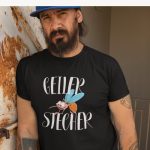 Schwarzes T-Shirt mit der lustigen Illustration einer breit grinsenden Mücke mit großen Augen und hellblauen Flügeln, umrahmt von dem geschwungenen weißen Schriftzug „GEILER STECHER“.