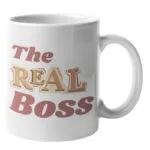 Weiße Keramiktasse mit seitlichem Henkel und dem mehrfarbigen Schriftzug „The Real Boss“ in Retro-Buchstaben auf der Vorderseite.