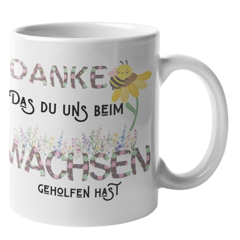 Weiße Tasse mit der Aufschrift „DANKE DAS DU UNS BEIM WACHSEN GEHOLFEN HAST“. Die Buchstaben der Wörter „DANKE“ und „WACHSEN“ sind mit bunten Blumenmustern gefüllt. Über dem Text ist eine kleine, lächelnde Biene auf einer gelben Blume zu sehen, und im unteren Bereich befinden sich Illustrationen von verschiedenen Wildblumen.
